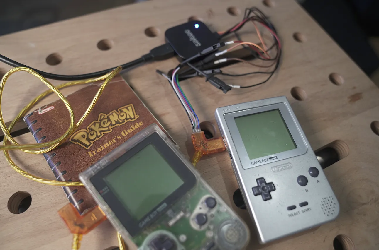 Two Game Boys hooked up with a link cable, with a Pokémon Trainer's Guide in the background